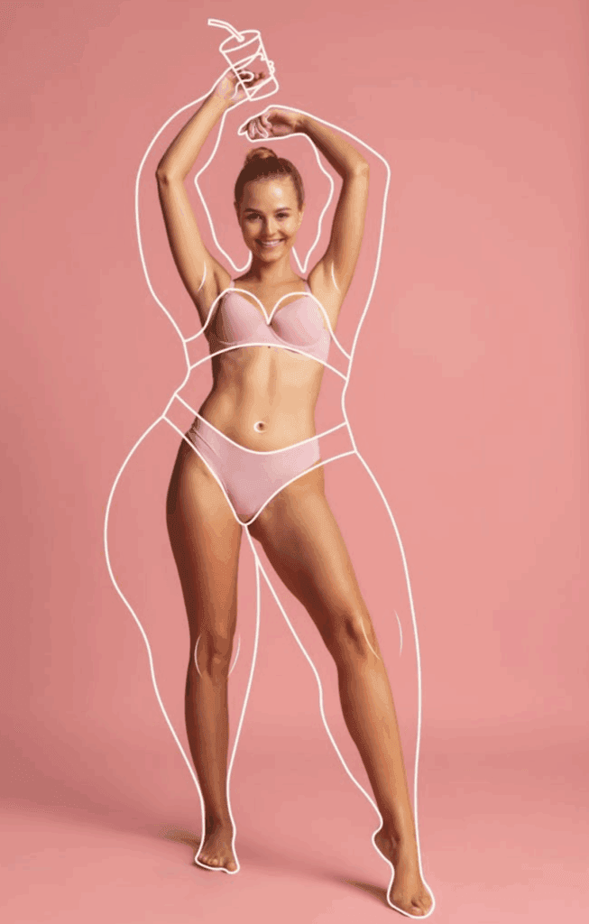 A studio portrait of a woman with an athletic build, smiling and posing with arms raised, wearing light pink lingerie. Her makeup is natural and dewy, and the lighting is soft and even. A white, hand-drawn outline overlay depicts a fuller, curvier feminine silhouette surrounding her body, emphasizing body positivity against a solid soft pink background.