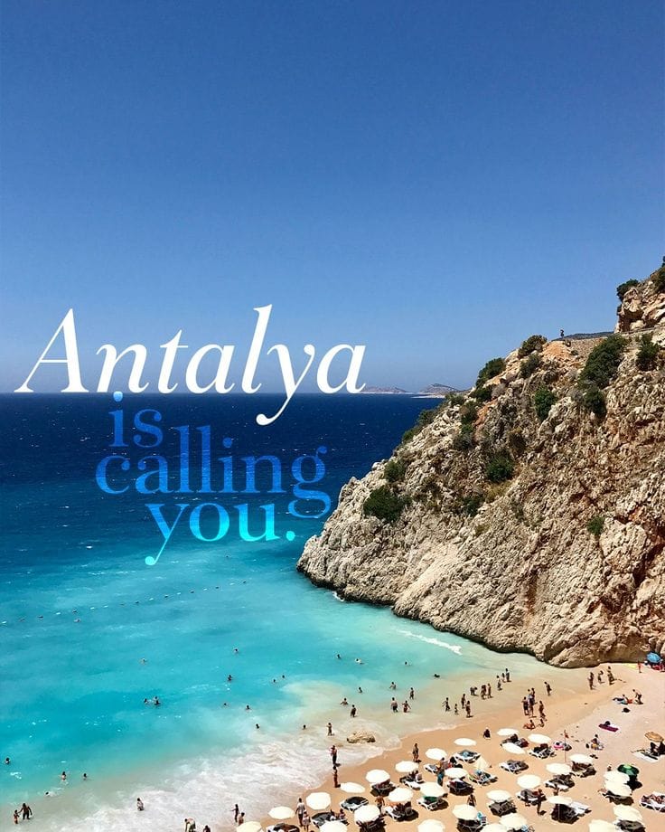 A vibrant travel-inspired image showcasing a breathtaking beach in Antalya, Turkey. The scene features a stunning turquoise sea meeting a sandy beach filled with people enjoying the sun. The rocky cliffs on the right side add a natural contrast to the serene blue waters. The sky above is clear and bright, enhancing the inviting atmosphere of the beach. The overlaid text reads 'Antalya is calling you.' in a stylized font. Details for accessibility and context: - **Lighting**: The image is captured in bright daylight, highlighting the vivid colors of the sea, sky, and beach. - **Makeup**: Not applicable, as there are no close-up subjects or individuals visible. - **Masculine/Feminine Elements**: Not applicable, as the focus is on the landscape and scenery. - **Background**: The background features a clear blue sky, turquoise sea, rocky cliffs, and a sandy beach with people and umbrellas. - **Anatomy**: Not applicable, as there are no detailed human figures visible. - **Clothing Details**: People on the beach are seen wearing typical beachwear such as swimsuits, shorts, and sun hats, though no specific details are discernible due to the distance.